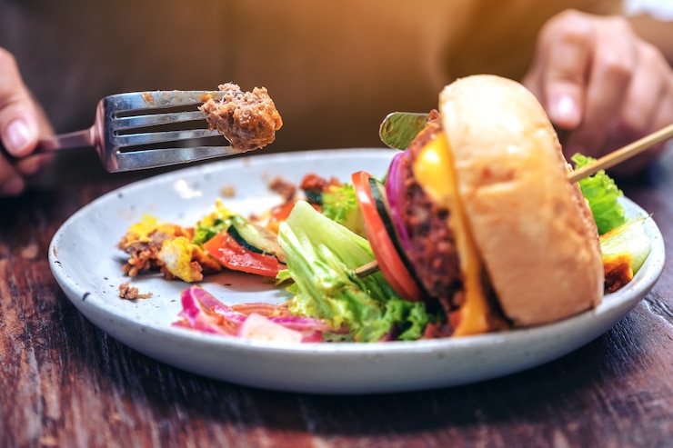 Foto frau, die rindfleischhamburger mit messer und gabel im restaurant isst
