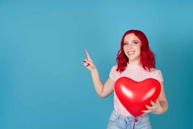 Frau, die roten fliegenden Ballon in der Form des Herzens hält und Zeigefinger auf leeren Raum für Text zeigt