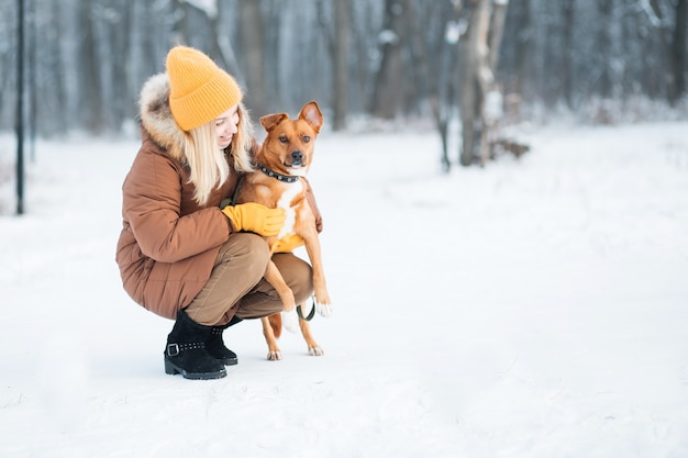 Frau, die roten Mischlingshund im Winterwald umarmt