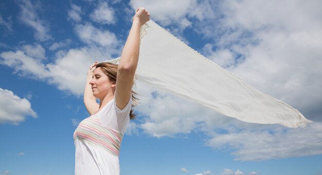 Frau, die Schal gegen blauen Himmel und Wolken hält