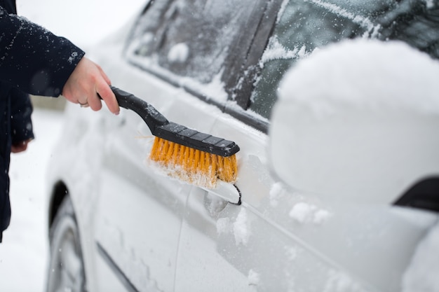 Frau, die Schnee vom Auto im Winter reinigt. Autogriff.