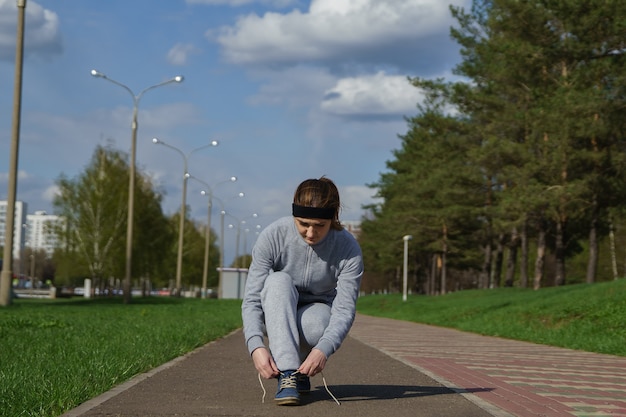 Frau, die Schnürsenkel bindet. Weiblicher Sport-Fitness-Läufer, der sich im Frühjahr oder Sommer zum Joggen im Freien auf dem Waldweg bereit macht.