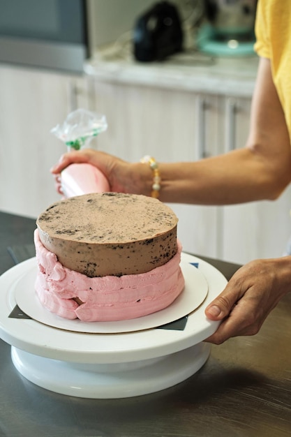 Frau, die Schokoladenkuchen mit rosa Sahnenahaufnahme macht Kuchenherstellungsprozess Selektiver Fokus