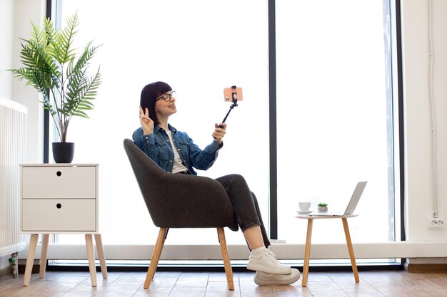 Frau, die selfie mit vsign unter verwendung des telefonsticks im büro macht