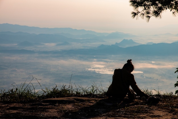 Frau, die serenely von der Klippe sitzt und morgens das Tal und die Berge betrachtet