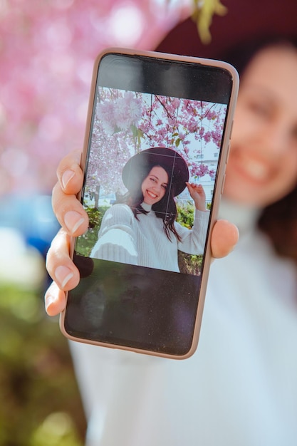 Frau, die sich am Telefon unter blühendem Sakura-Baum-Selfie-Bild erschießt