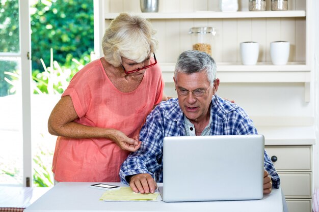 Frau, die sich bei Tisch mit älterem Mann auf Laptop bespricht