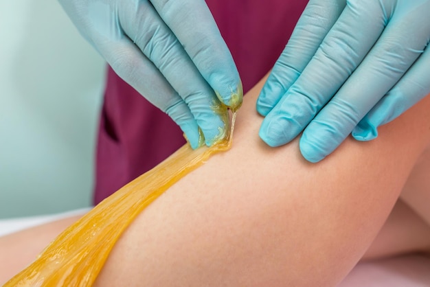 Frau, die sich einer Beinhaarentfernung mit Zuckerpaste im Salon unterzieht Hautpflege Haare mit Zuckerpaste entfernen