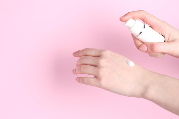 Frau, die sich gegen einen rosa Hintergrund eine Creme auf die Hand legt, Nahaufnahme Platz für Text