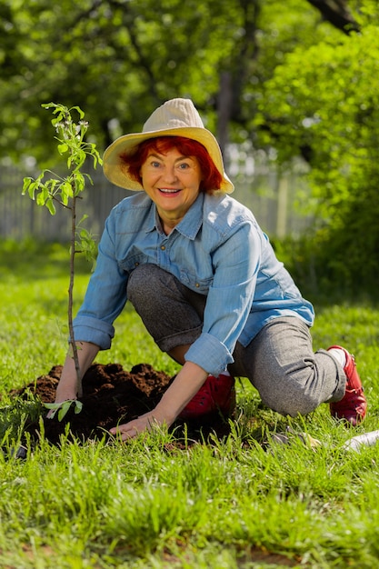 Frau, die sich glücklich fühlt. Strahlende glückliche rothaarige Rentnerin, die sich nach dem Pflanzen des Baumes glücklich fühlt