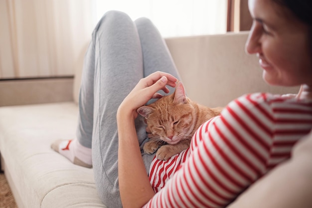 Frau, die sich mit ihrem Ingwer-Haustier auf einem Sofa entspannt Gemütliches Szene-Hygge-Konzept