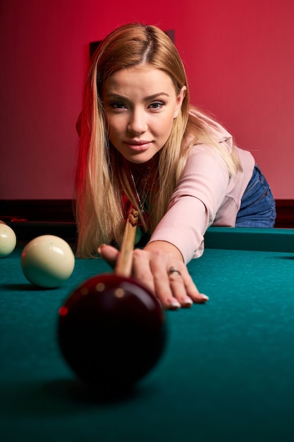 Frau, die sich über den Tisch beugt, während sie Snooker spielt, genießt die Freizeit, Billard zu spielen
