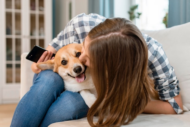 Frau, die Smartphone hält und ihren Hund küsst