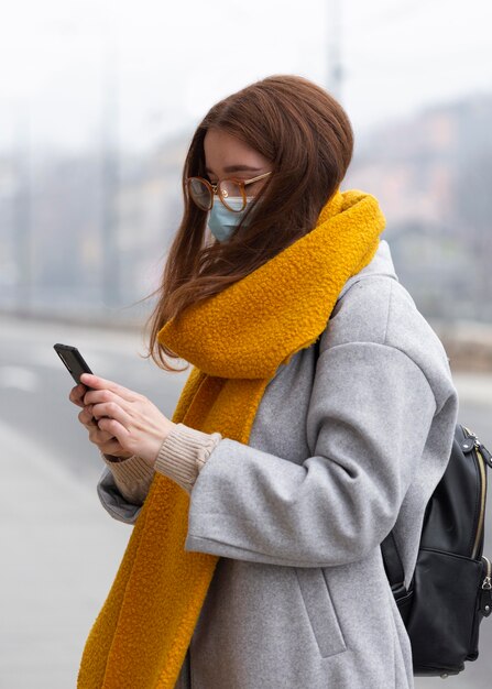 Frau, die Smartphone in der Stadt beim Tragen der medizinischen Maske verwendet