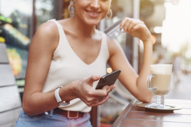 Frau, die Smartphone und eine Kreditkarte für Online-Einkauf hält.