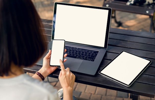 Frau, die Smartphone- und Tablet-Bildschirm leer mit Laptop auf dem Tisch hält, verspotten, um Ihre Produkte zu fördern.