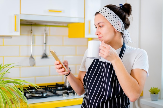 Frau, die Smartphone verwendet und Kaffee in der glücklichen Morgenfreizeit des Küchenkonzeptes trinkt