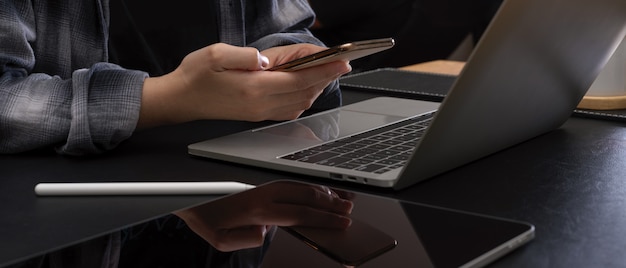 Frau, die Smartphone während der Arbeit am Schreibtisch verwendet