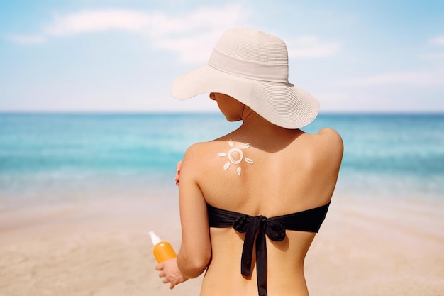 Frau, die Sonnencreme auf gebräunte Schulter in Form der Sonne aufträgt SonnenschutzSonnencreme Haut