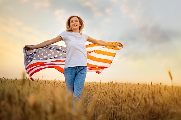 Frau, die sorglos mit offenen Armen über Weizenfeld läuft, das eine USA-Flagge hält