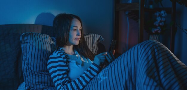 Frau, die spät in der Nacht im Bett liegt und ihr Telefon benutzt, um im Internet zu surfen