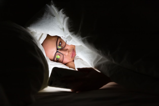 Frau, die spät in der Nacht im Bett mit Smartphone liegt. Schlaflosigkeit, Nomophobie, Schlafstörung.