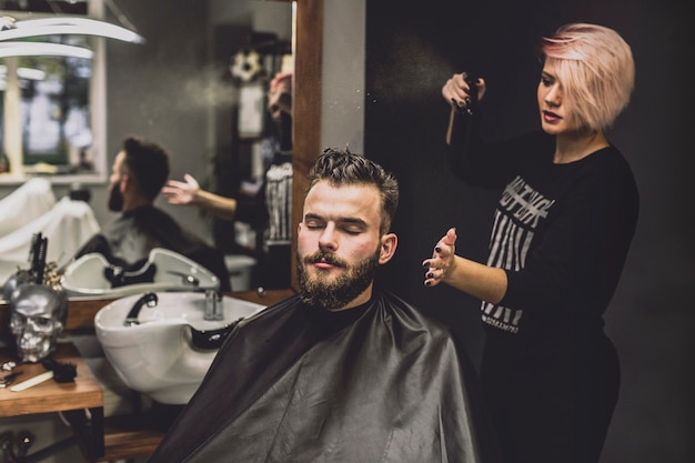 Frau, die Spray auf Mann im Friseursalon verwendet