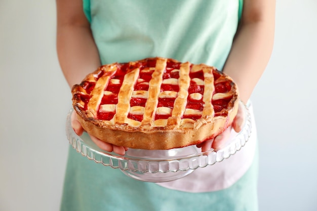 Frau, die Stand mit köstlichem Erdbeerkuchen auf hellem Hintergrund hält