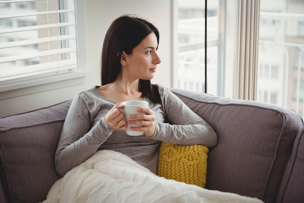 Frau, die Tasse hält, während sie durch Fenster schaut