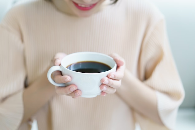 Frau, die Tee oder Kaffee trinkt. Weiße Tasse heißes Getränk am Morgen.