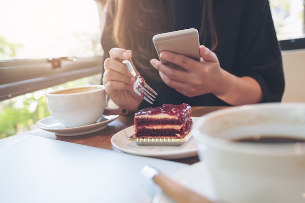 Frau, die Telefon mit dem Essen des Kuchens verwendet