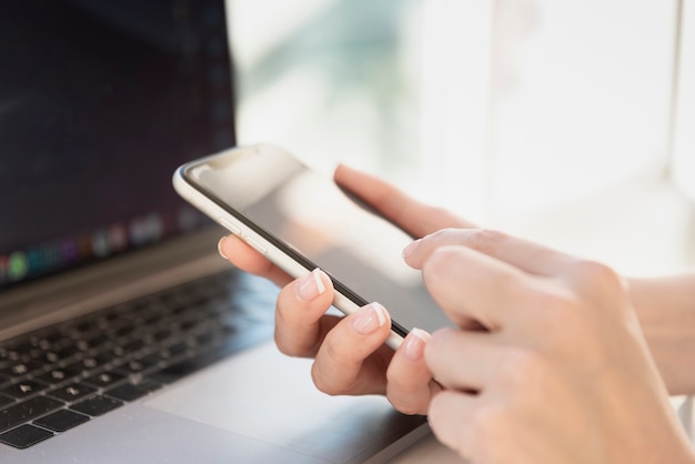 Frau, die Telefon mit Laptop im Hintergrund hält