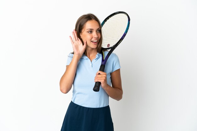 Frau, die Tennis über isolierte weiße Wand spielt, die etwas hört, indem man Hand auf das Ohr legt