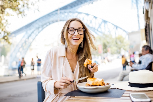 Frau, die traditionelles portugiesisches Sandwich mit Fleisch namens francesinha isst, das im Restaurant in der Stadt Porto, Portugal sitzt?