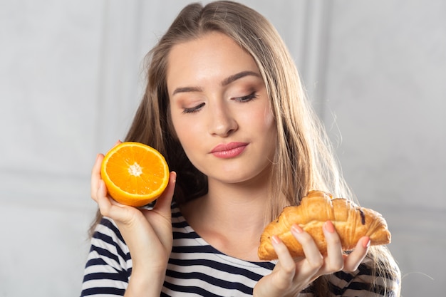 Frau, die ungesunden Kuchen und Orangenfrucht vergleicht