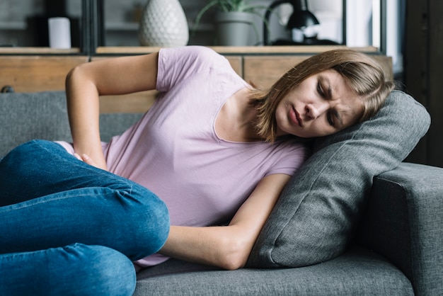 Foto frau, die unter den magenschmerzen liegen auf sofa leidet