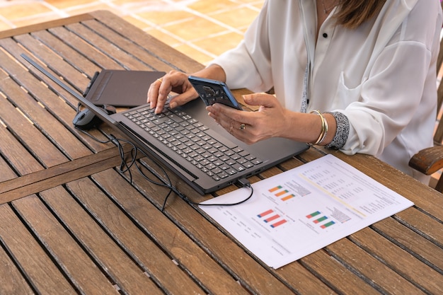 Frau, die von zu Hause aus im Garten mit Laptop und Handy arbeitet.