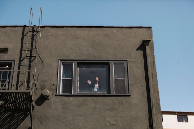 Frau, die während der Covid-19-Pandemie aus dem Fenster ihrer Wohnung in der Innenstadt von LA schaut