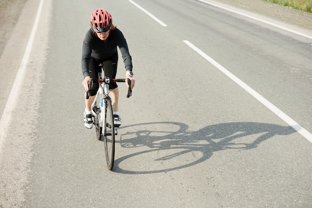 Frau, die während des Sporttrainings auf der sonnigen Straße oder der Autobahn des Landsommers radfährt