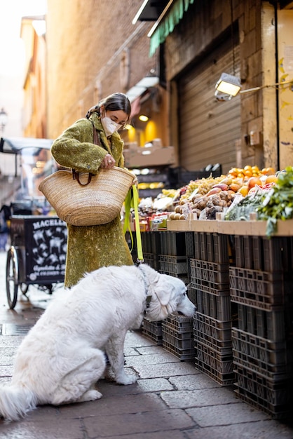 Frau, die während einer Pandemie mit einem Hund Lebensmittel auf dem Straßenmarkt kauft