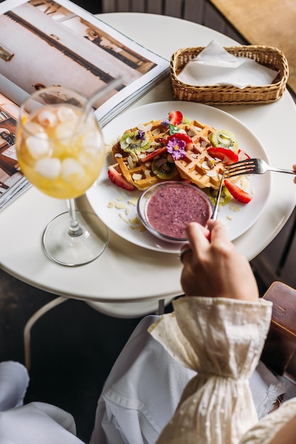 Frau, die Waffeln mit Erdbeeren und Früchten isst