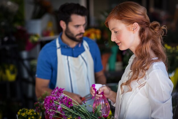 Frau, die Wasser auf Blumenstrauß sprüht, während Mann Blumenstrauß vorbereitet