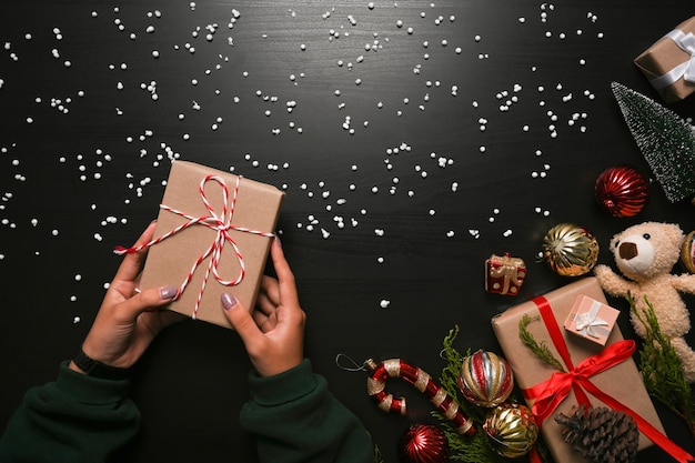 Frau, die Weihnachtsgeschenkbox auf dunklem Hintergrund hält.