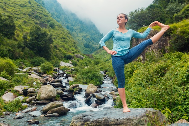 Frau, die Yoga asana draußen am Wasserfall tut