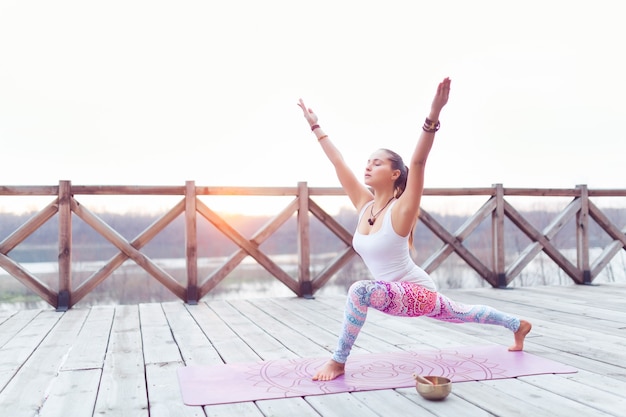 Frau, die Yoga im Freien über Himmel und Holzbrückenhintergrund praktiziert, kopieren Raumkonzept.
