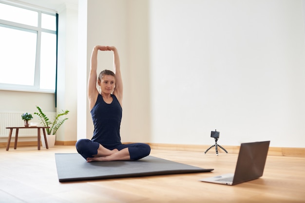 Frau, die Yoga online macht. Computer und Kamera in ihrem Wohnzimmer. Konzepte für einen gesunden Lebensstil und Fernarbeit