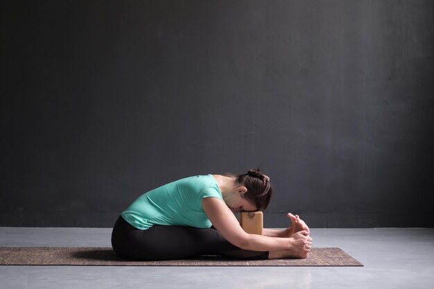 Frau, die Yoga praktiziert Sitzende Vorwärtsbeuge-Pose mit Ziegeln oder Blöcken