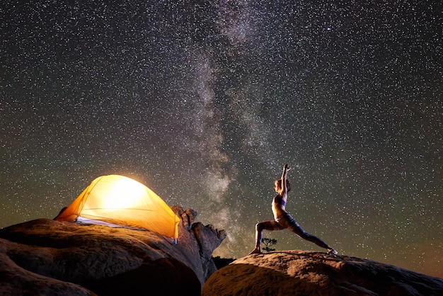 Frau, die Yogaübungen auf Berggipfel in der Nacht tut