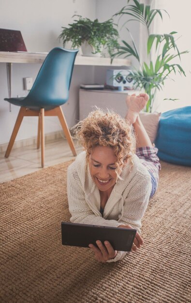 Frau, die zu Hause auf dem Teppichboden liegt und ein Laptop-Gerät mit Internet-Webverbindung verwendet. Frauen surfen und genießen die Kommunikation. Eine Person mit Technologie