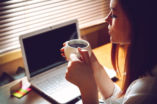 Frau, die zu Hause Büro mit Tasse Kaffee sitzt